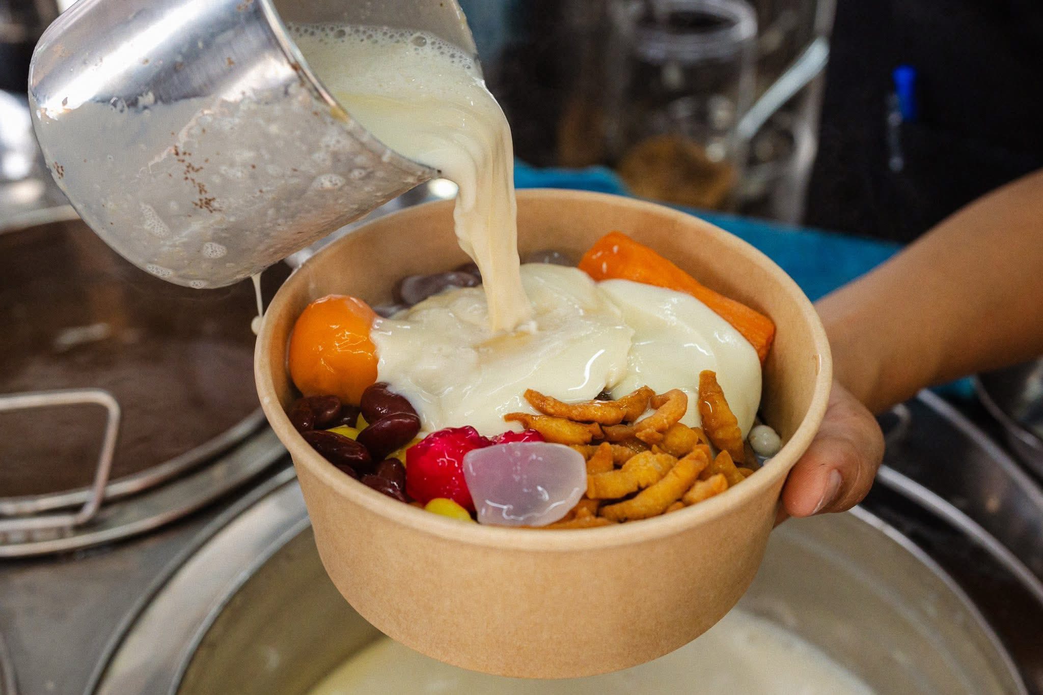 น้ำเต้าหู้ร้อนๆ กำลังถูกรินลงบนเต้าฮวยและเครื่องธัญพืช